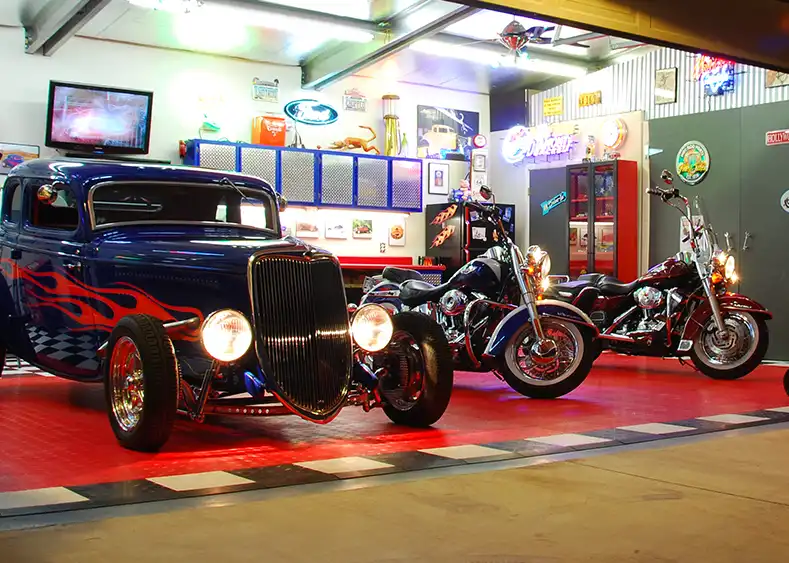 A garage at night with a hotrod coupe and two Harley Davidson motorcycles and RaceDeck garage floor tiles on concrete.