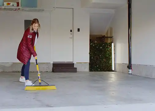 A young woman sweeps out her garage before she installs her garage floor tiles.
