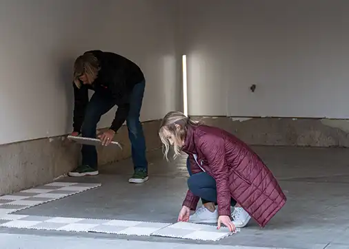 A young woman and her dad install RaceDeck garage flooring tiles.