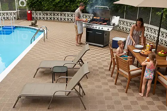A family grills poolside.The deck is covered with Free-Flow deck tiles